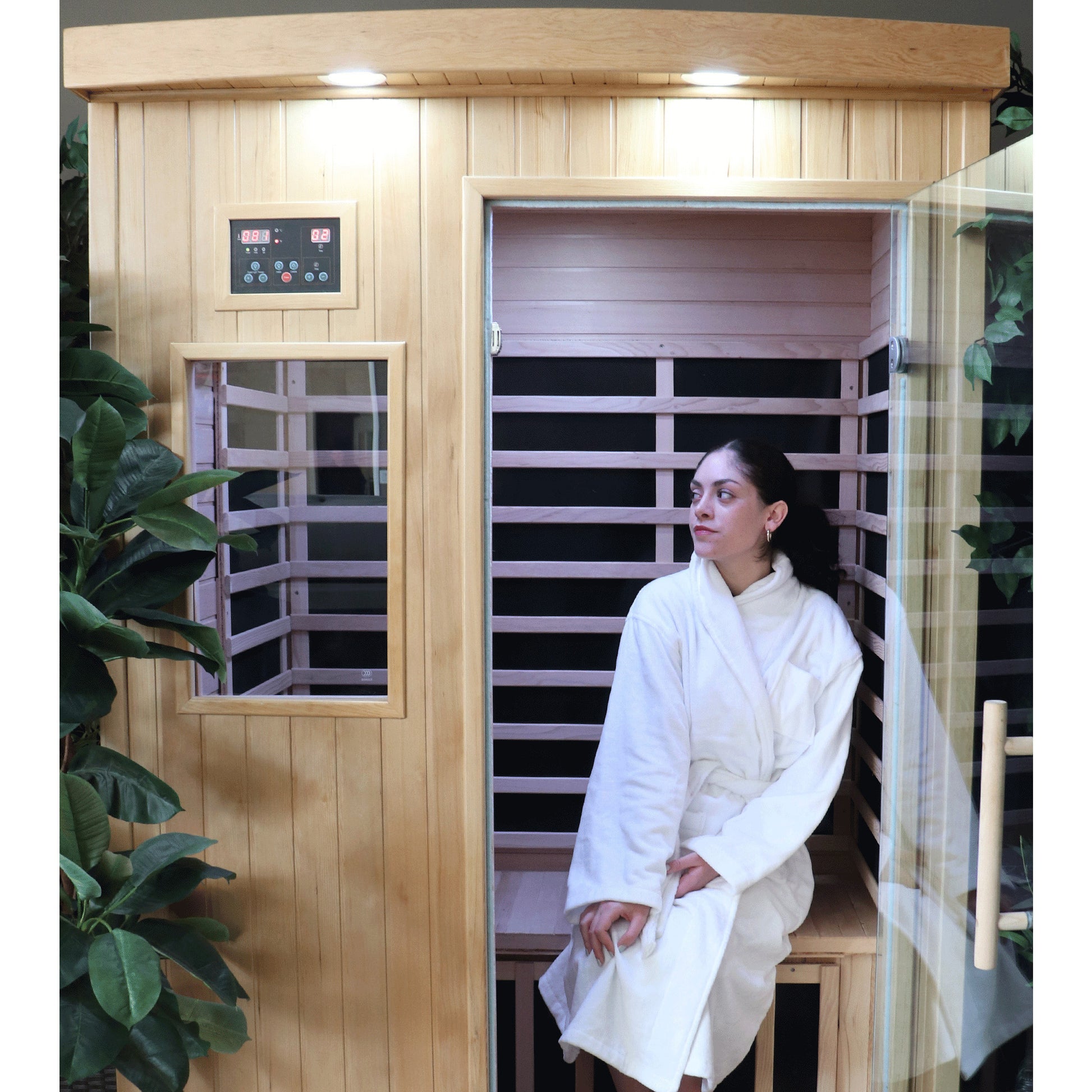 Person in a white robe sitting inside a wooden infrared sauna.