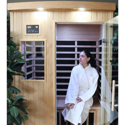 Person in a white robe sitting inside a wooden infrared sauna.